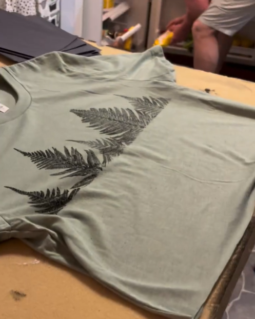 Thumbnail: real ferns stamped with black ink onto this youth green shirt.
