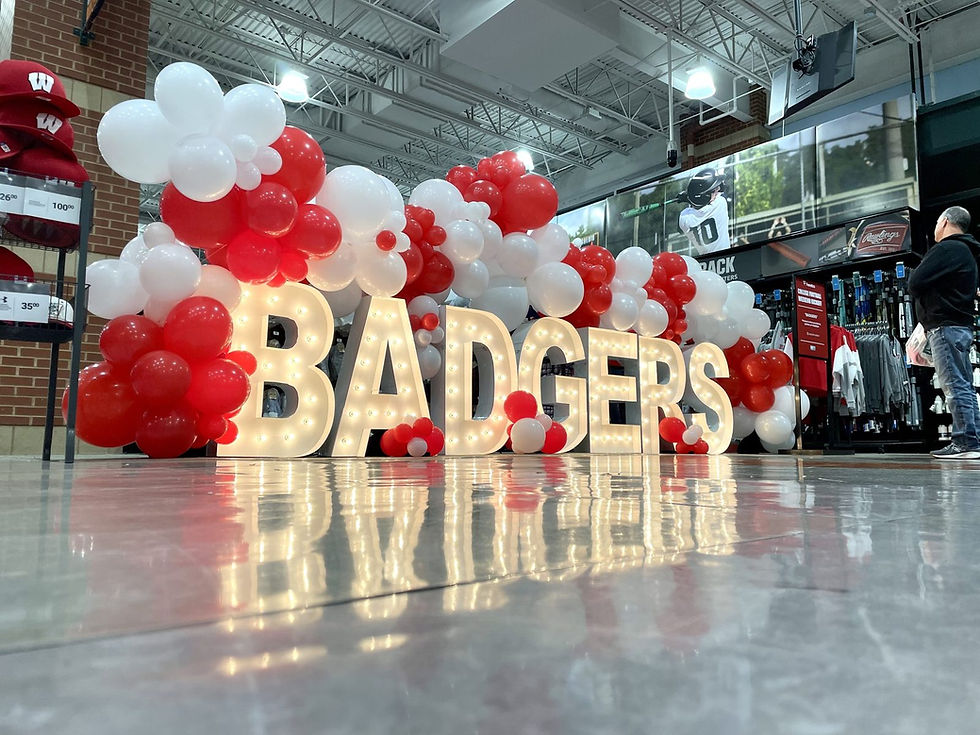 Lighted marquee letters spelling BADGERS with red and white organic balloon garland.