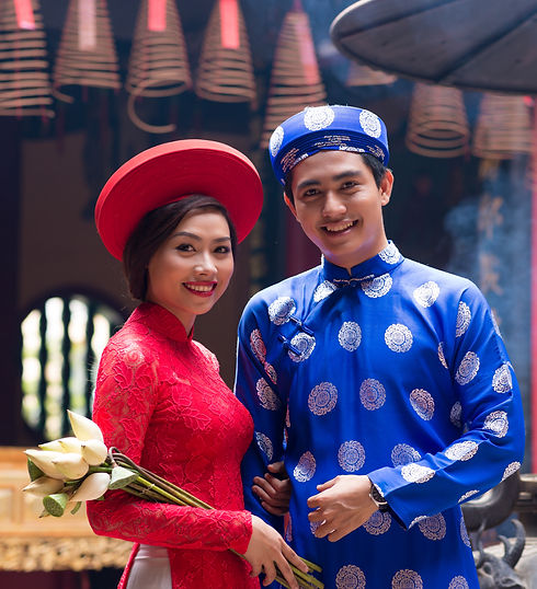 Vietnamese bride and groom in traditional áo dài wedding attire - bride wearing red embroidered dress with matching hat, groom in blue silk áo dài with decorative patterns and traditional cap