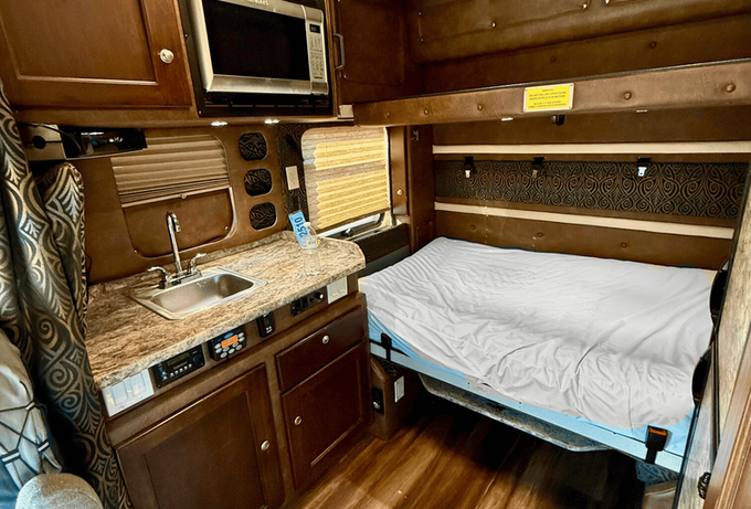Looking into a custom sleeper from the cab of an expediter truck showing the counter tops, convection oven, and sink. 