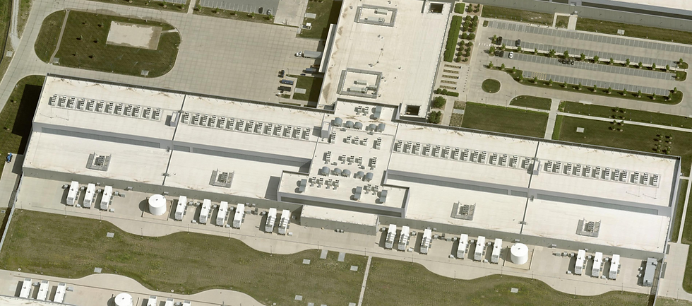 Meta Sarpy County Campus, 14734 Friend Plaza, Springfield, Nebraska. The overhead perspective lays bare the mechanical logic of hyperscale computing. Stretching across the frame is a single data hall module — its roofline consumed by parallel rows of air-side economizer units, the signature cooling architecture Meta pioneered through the Open Compute Project. The dense white arrays flanking the building's perimeter are diesel backup generators, each one a self-contained power island engineered to sustain full load within seconds of a grid interruption. Two cylindrical white tanks — thermal buffer storage for the cooling system — anchor the southern apron. The manicured green setbacks and structured parking visible to the upper right are characteristic of Meta's campuses: designed not for aesthetic appeal but for emergency vehicle access radii and future expansion clearance. What the image cannot convey is scale — this single structure exceeds 1.1 million square feet, roughly equivalent to 19 football fields under one roof. Photo taken May 8, 2025, Source: MMCG Invest, LLC/EagleView