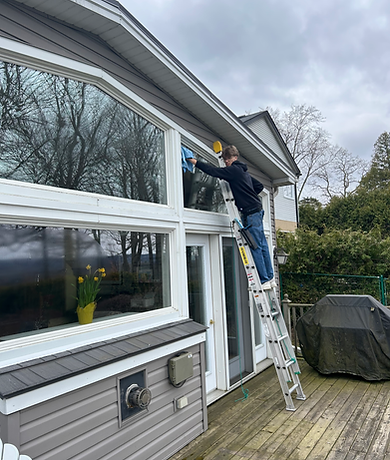 A man on a ladder using a window washing mop to clean windows