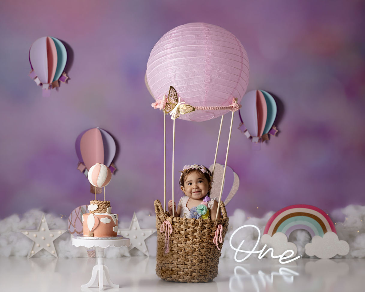 Baby girl enjoying a pink hot air balloon themed cake smash during her first birthday photoshoot in Orlando.