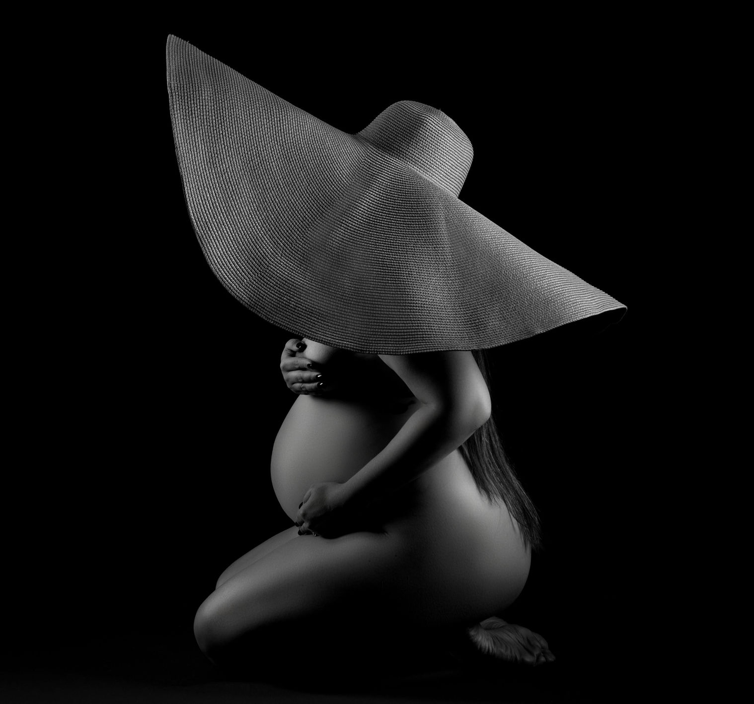 Pregnant woman wearing only a big straw hat during a maternity photography session in Orlando FL studio