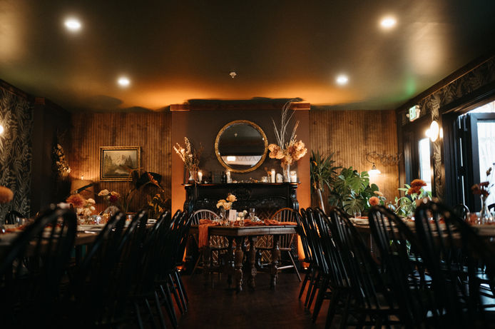 A warm and dimly lit room with dinner tables, a green ceiling, and a gilded round mirror on the wall.