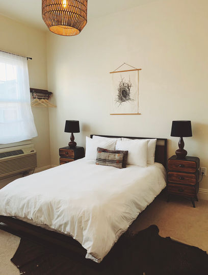 White bed, black lamps, sheer curtains, wood toned end tables.