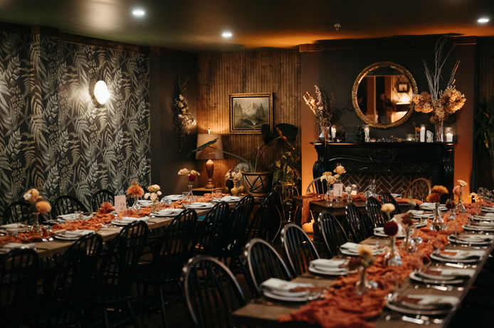 Warm and dimly lit dining room with 2 long, decorated dinner tables.