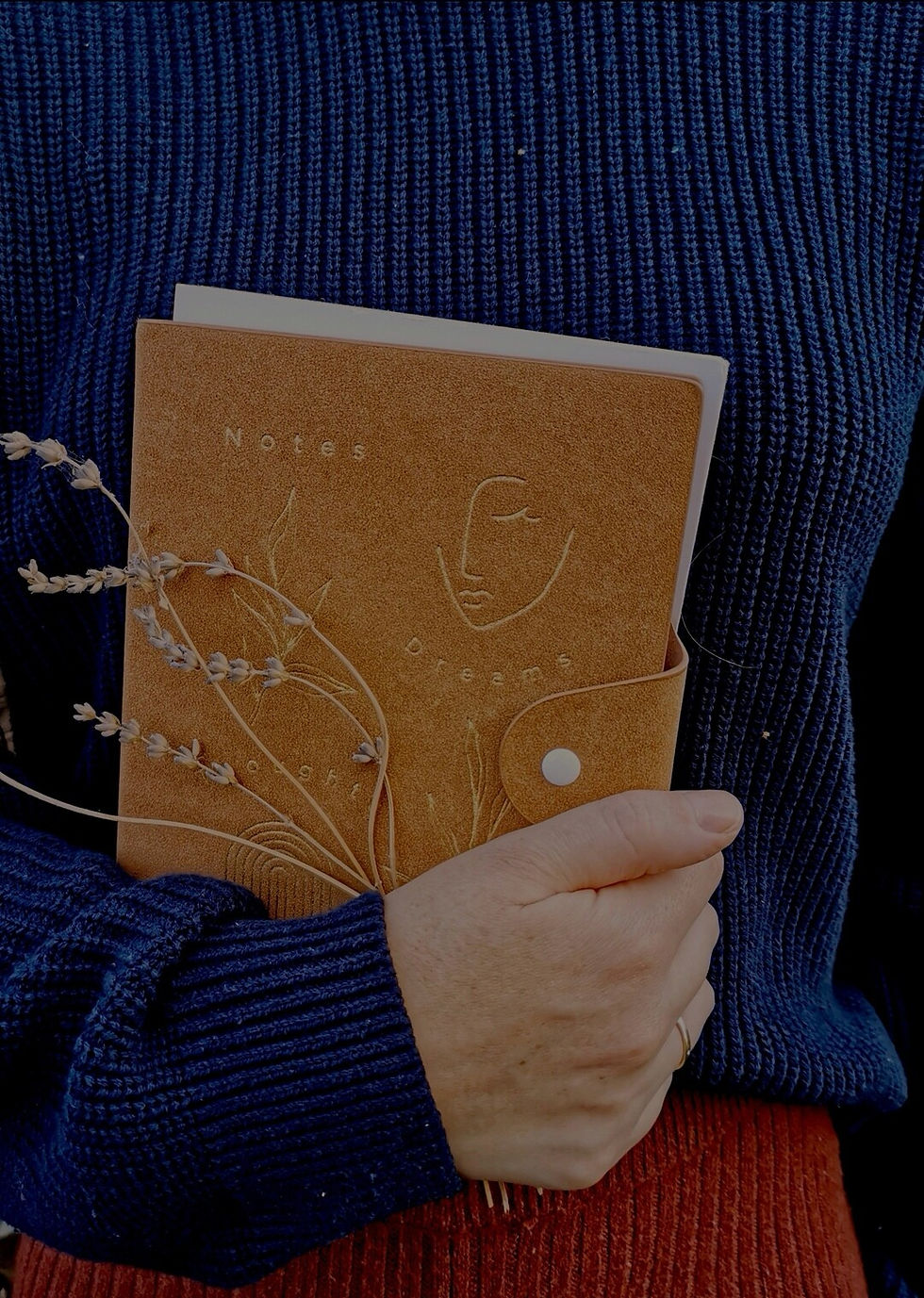 Woman in navy blue jumper holding brown notebook with some lavander.