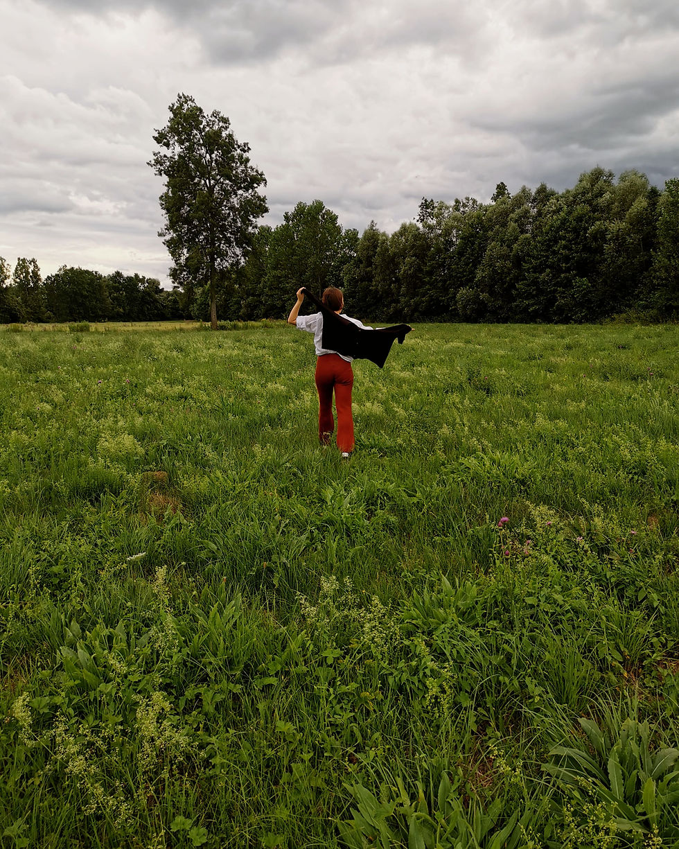 Woman in red pants, white shirt and black cardigan walking in the green meadow