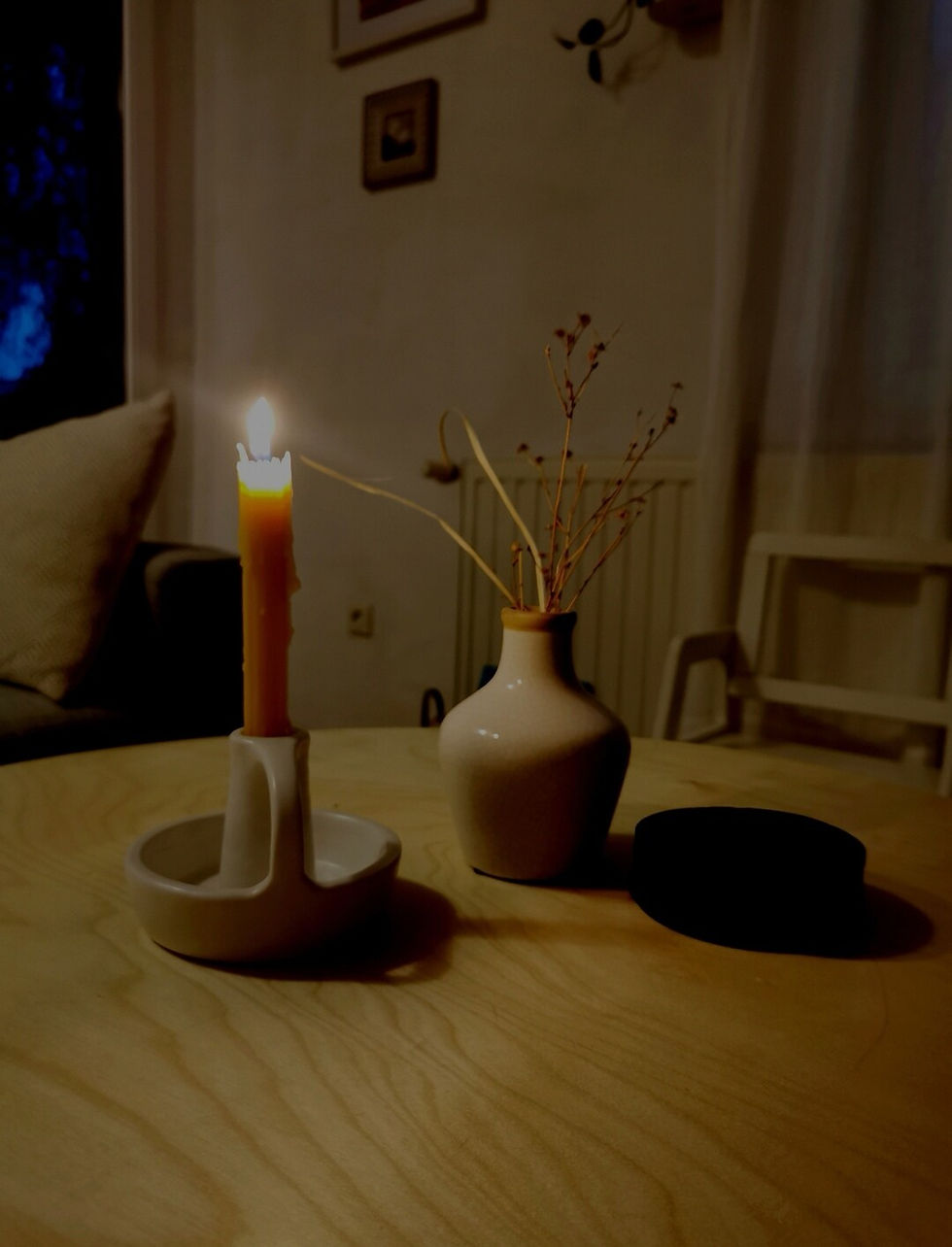 Candle lit in white candle holder on wooden table.