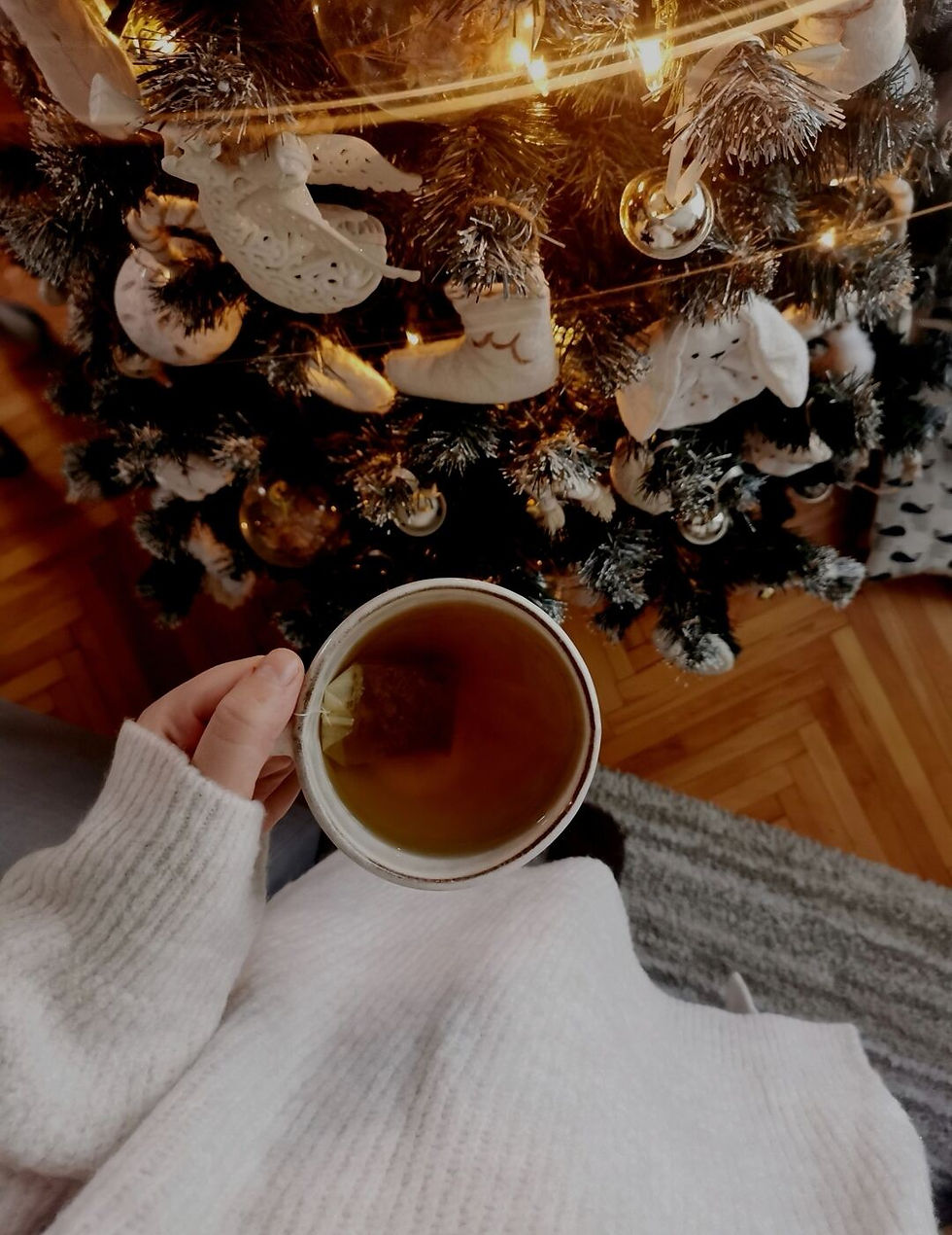 Woman hand in beige jumper holding mug of tea beside my Christmas tree.