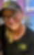 A smiling cafe employee wearing a black shirt and black hat, both featuring the yellow Crave Cafe lo