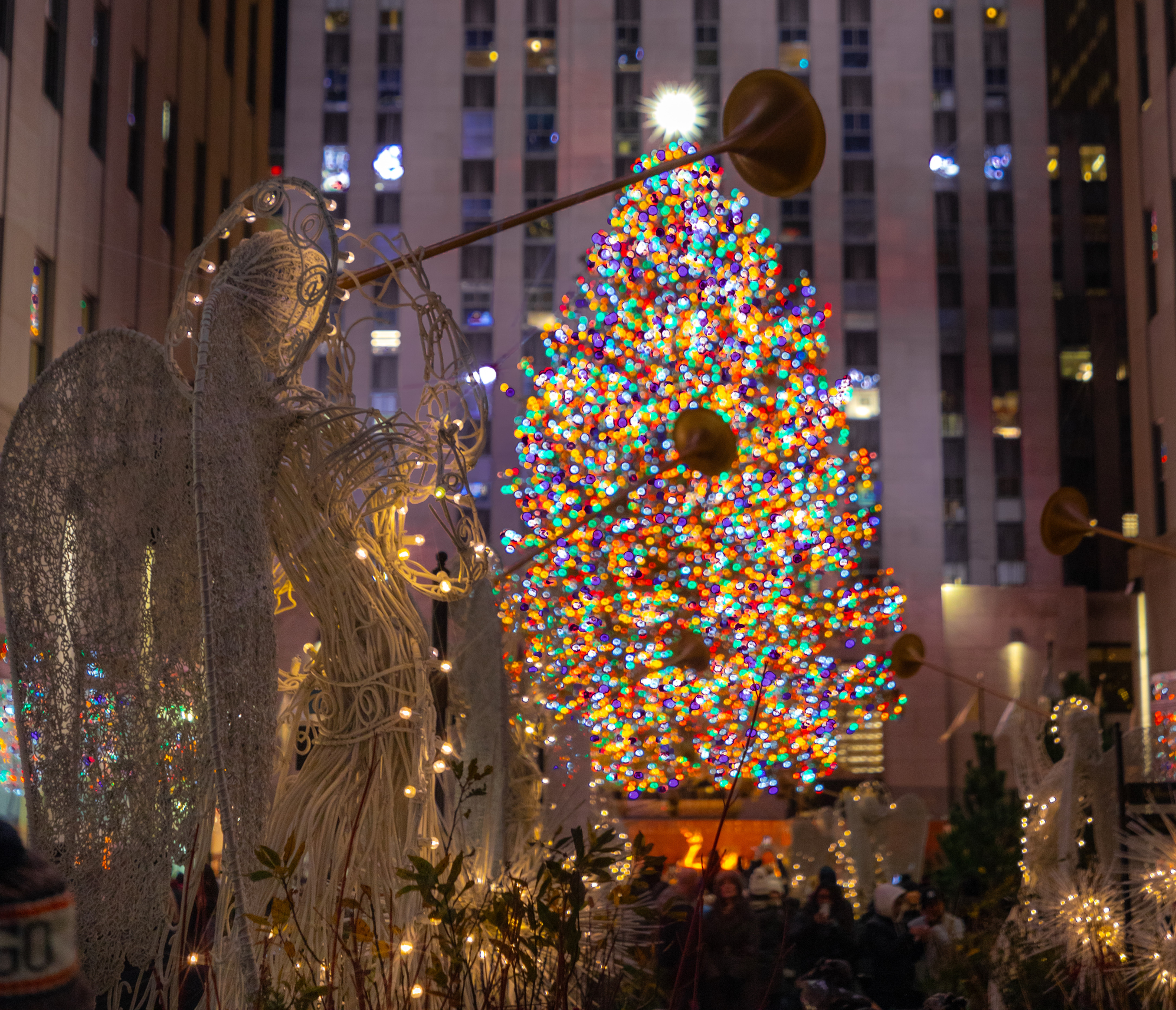 New York City, New York, USA; Hilton New York Midtown, Rockefeller Christmas Tree lit up with colorful lights, in front of the tree in a row of white angels with trumpets lit up with warm lights