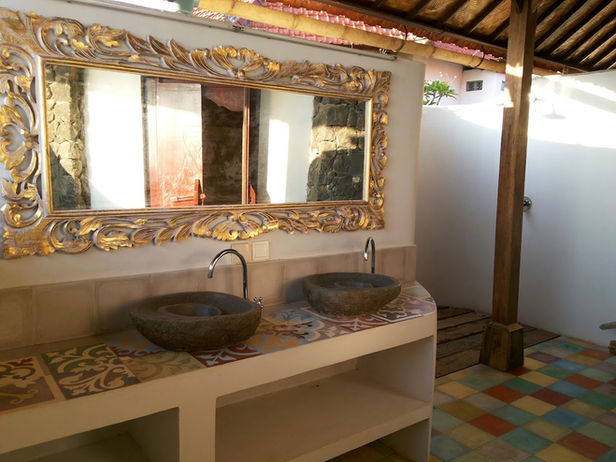 Balinesisches Badezimmer im Balila Beach Resort in Amed mit Naturstein-Waschbecken, kunstvoll verziertem Spiegel und offener Gestaltung.