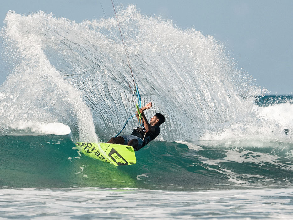 Kitesurfer performing a jump with a large water spray.