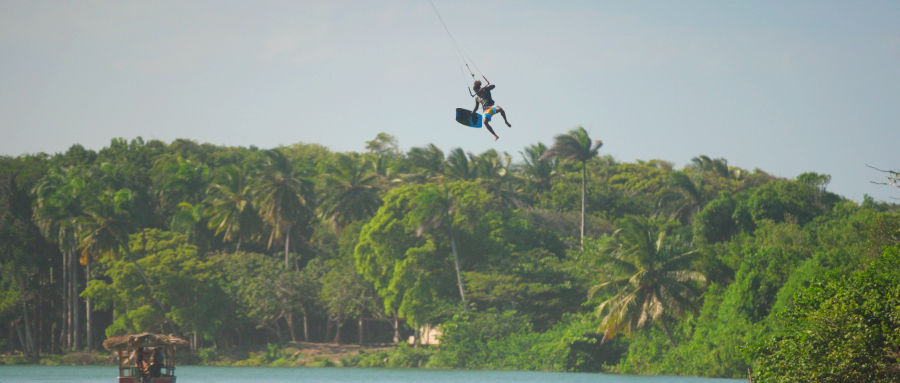 Kitesurfer performing a big-air jump above a palm-lined lagoon near Cabarete