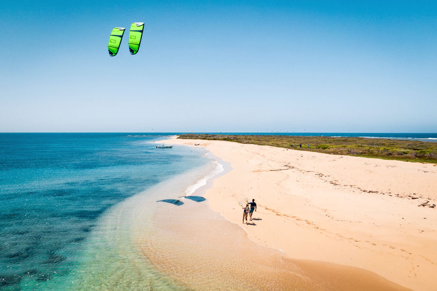 Two kites flying high above the cay as riders walk along the beach