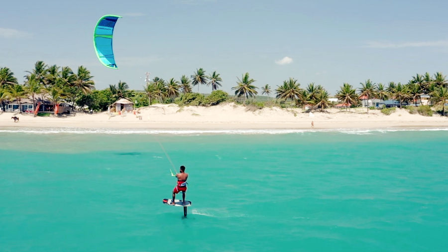Hydrofoil kiteboarder riding turquoise water near a beach hut in Cabarete