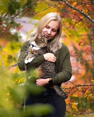 Nainen istuu hänen ruskea kissa sylissä syksyisessä ja värikkäässä metsässä