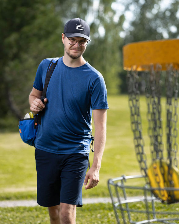 Sini paitainen frisbeegolffari frisbeekorin takana