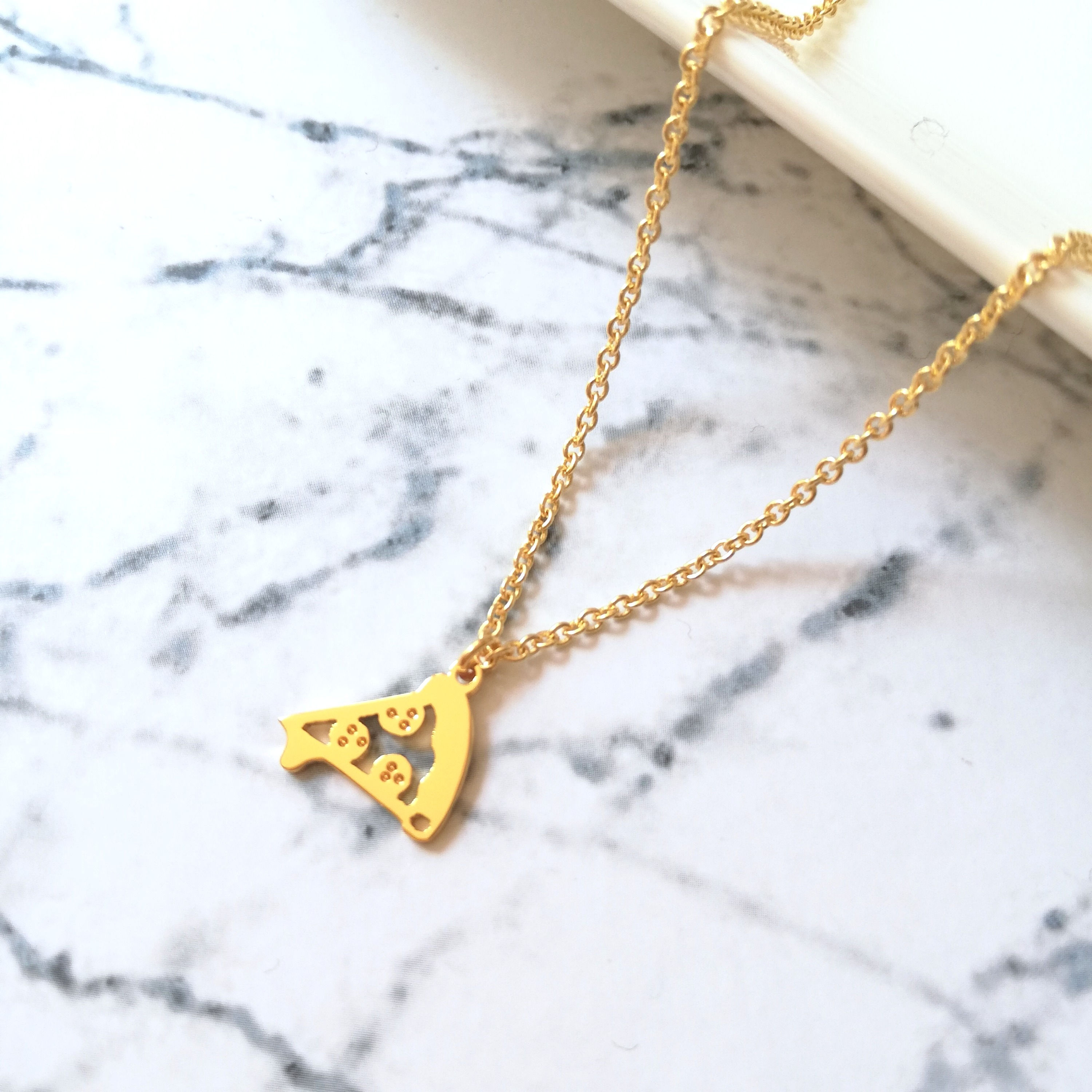 Gold slice of pizza necklace on marble. The pendant top is flat, cutout and shiny. Three pepperoni on it