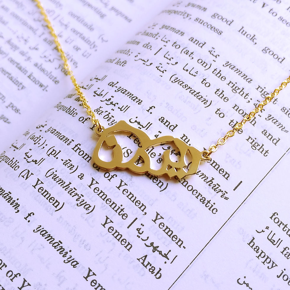 Thumbnail: Gold Yemen country shape necklace designed with Arabic word resting on dictionary page.