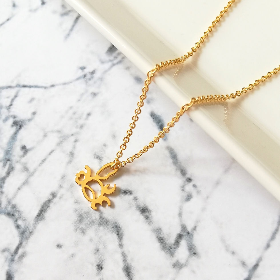 Thumbnail: Gold crab pendant laying on marble.The crab shape is formed with Arabic word.