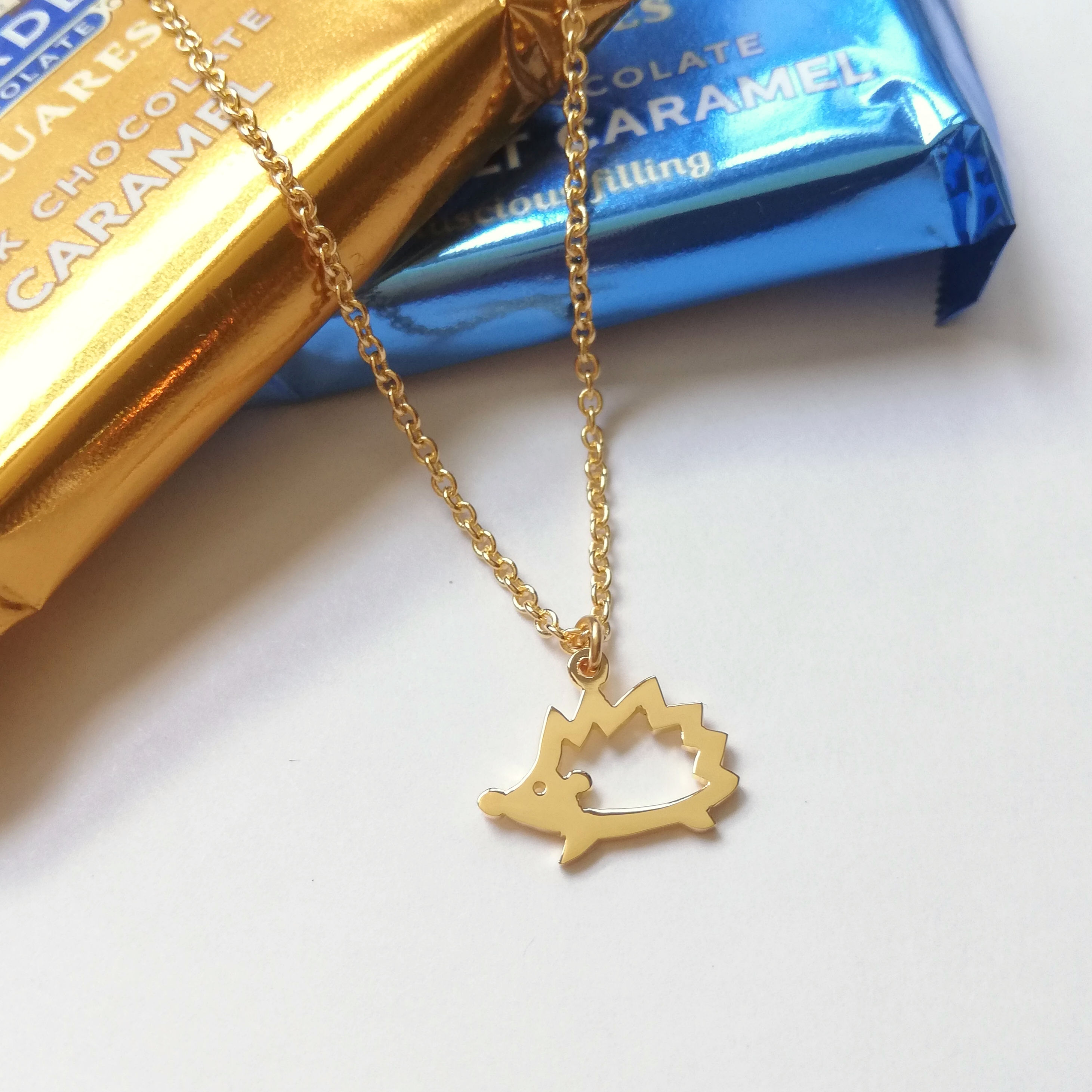 Gold hedgehog silhouette necklace hanging from chocolate packages.