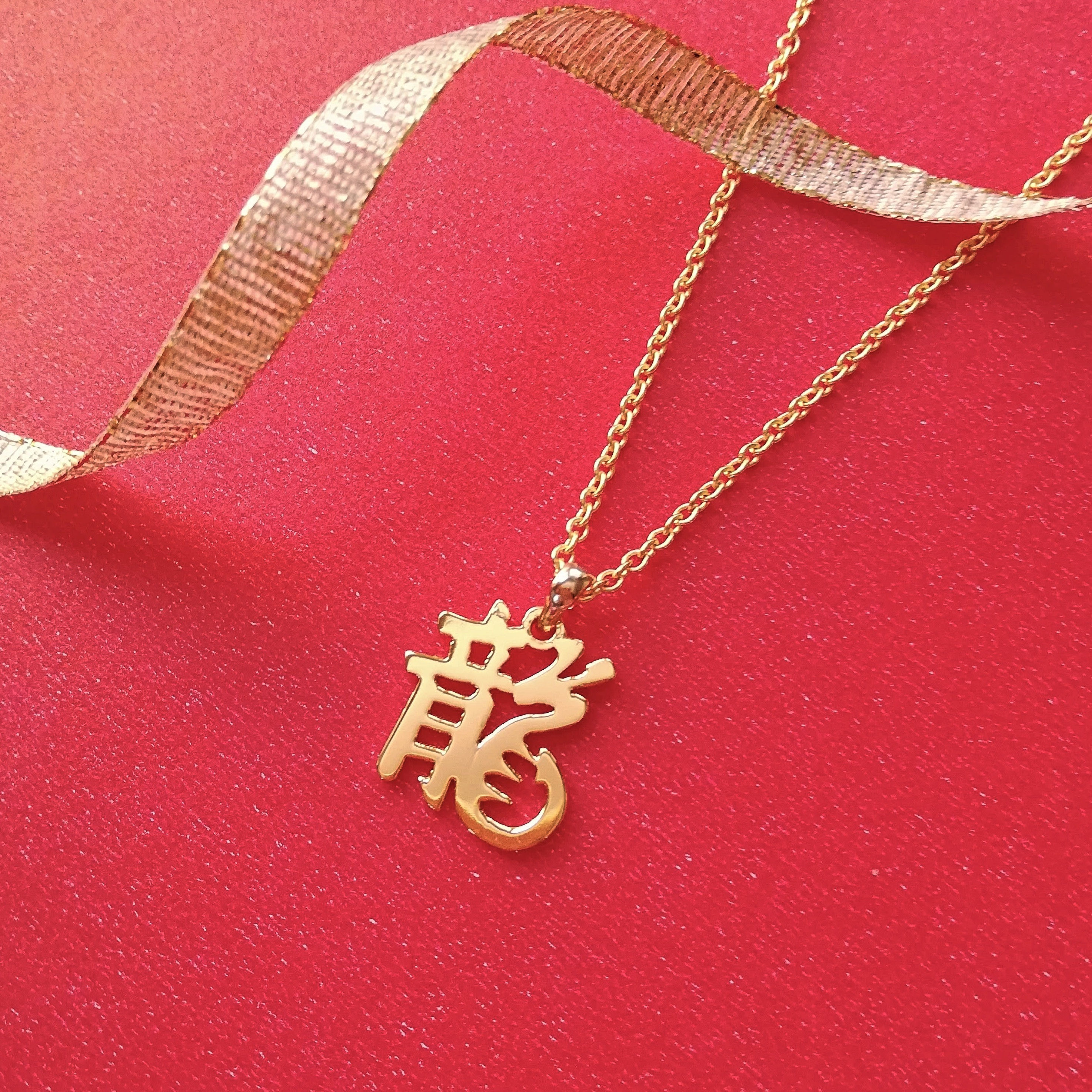 Gold Kanji 龍 Dragon necklace with right side converted to dragon shape lying on red with gold ribbon.