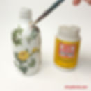 Applying Mod Podge over vellum stickers on a painted glass bottle during a DIY decoupage project