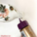 Adding glue to the neck of a decoupaged glass bottle to attach decorative trim.