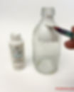 A hand painting a recycled glass bottle with white enamel paint as the first step in a DIY decoupage craft project.