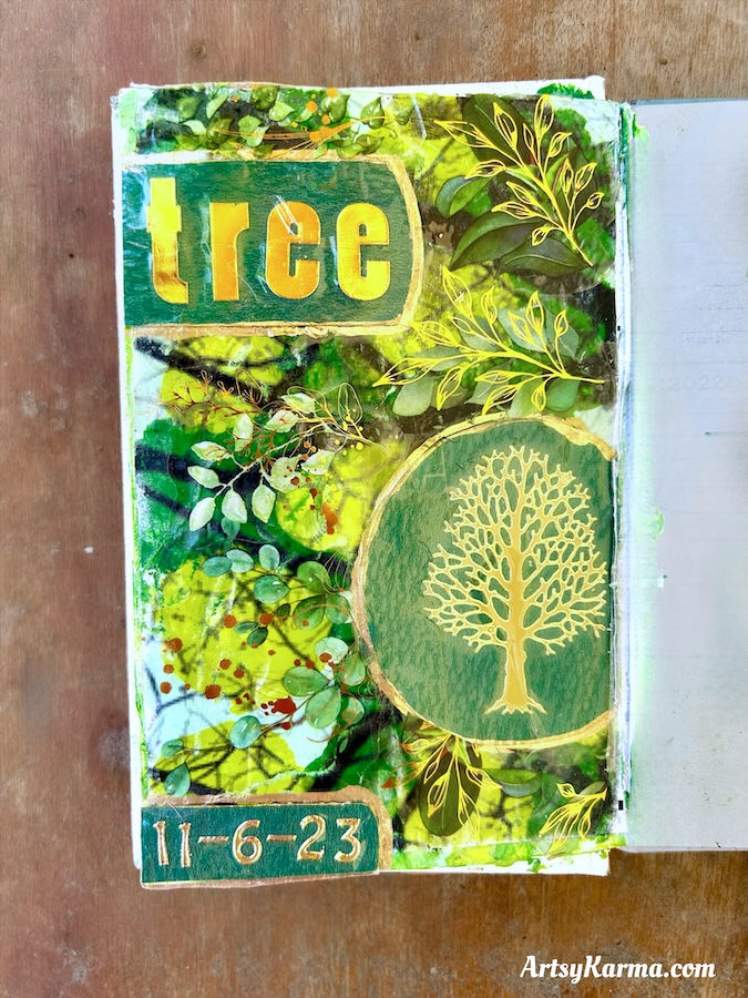 A finished art journal page with a completed acrylic paint image transfer, featuring added embellishments like a golden tree and the word 'tree.'