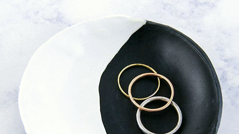 Black and white moon phase-inspired clay ring dish with a yin-yang pattern, holding three stacked rings on a marble background.