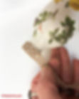 Attaching decorative ribbon trim to the top of a DIY decoupage bottle vase.