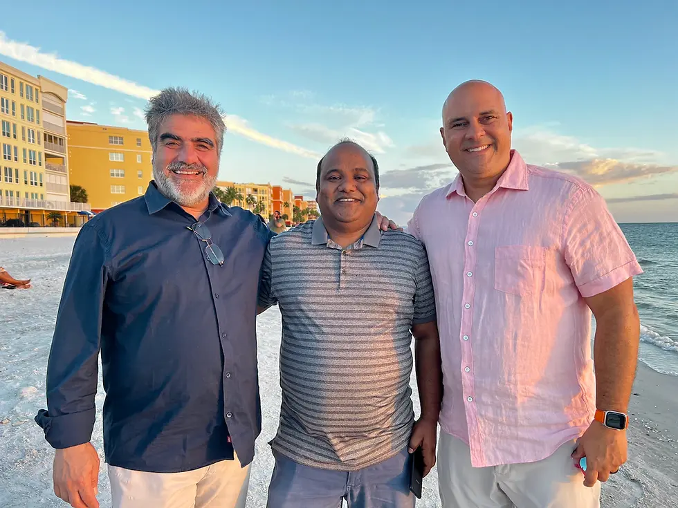 Three men stand with their arms around one another at a beach.