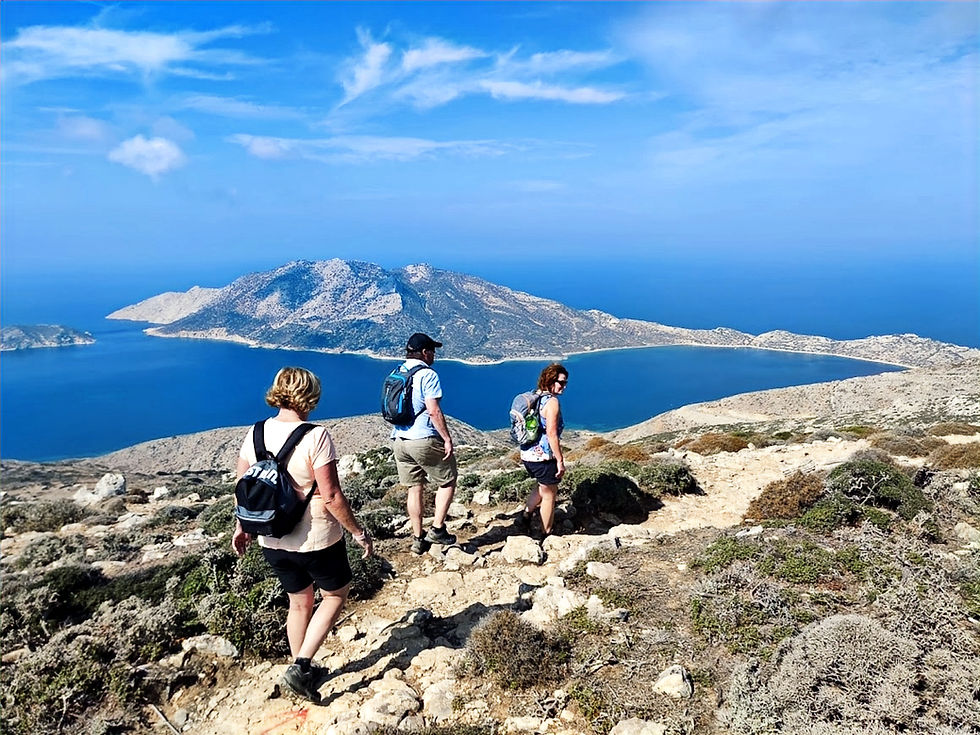 Three hikers descend a rocky trail above a bright blue bay and island under a clear sky.