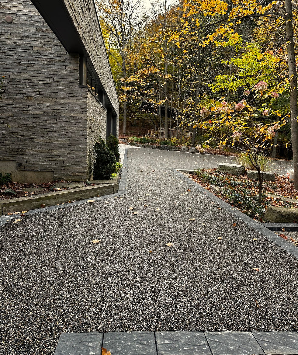 Outdoor resin bound driveway leading up to a modern stone house in the woods, autumn trees, landscape orientation.