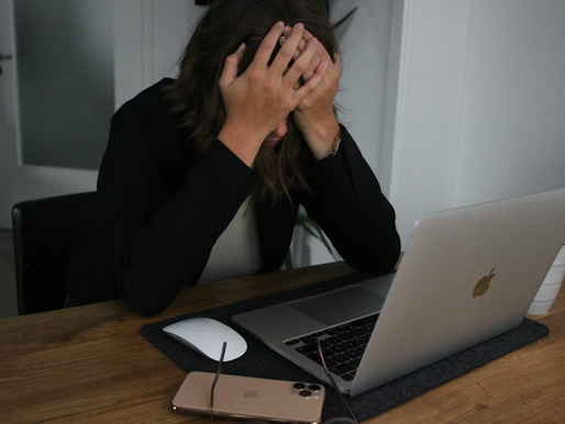 A young girl holding her head in her palms, with elbows balanced on a desk in front of a MacBook