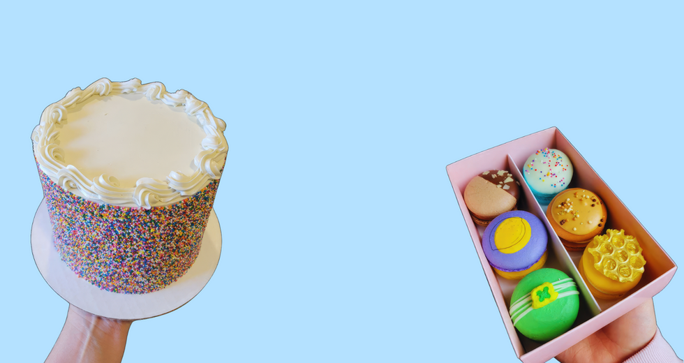 Hand holding cake and colorful macarons in a box, light blue background.