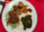 Plate of jollof rice, white rice, fried plantains, green sauce, and spinach stew on red tablecloth.