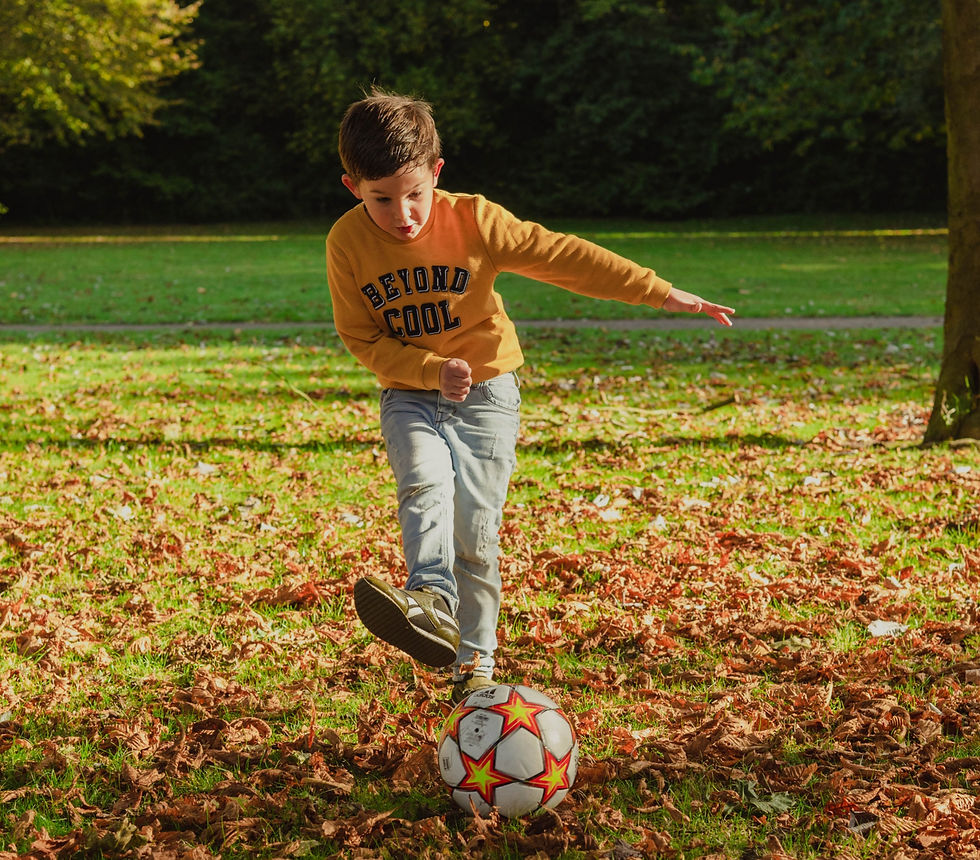 A young boy playing football amongst the Autumn Leaves. It's an action shot of him just after he's kicked the ball.