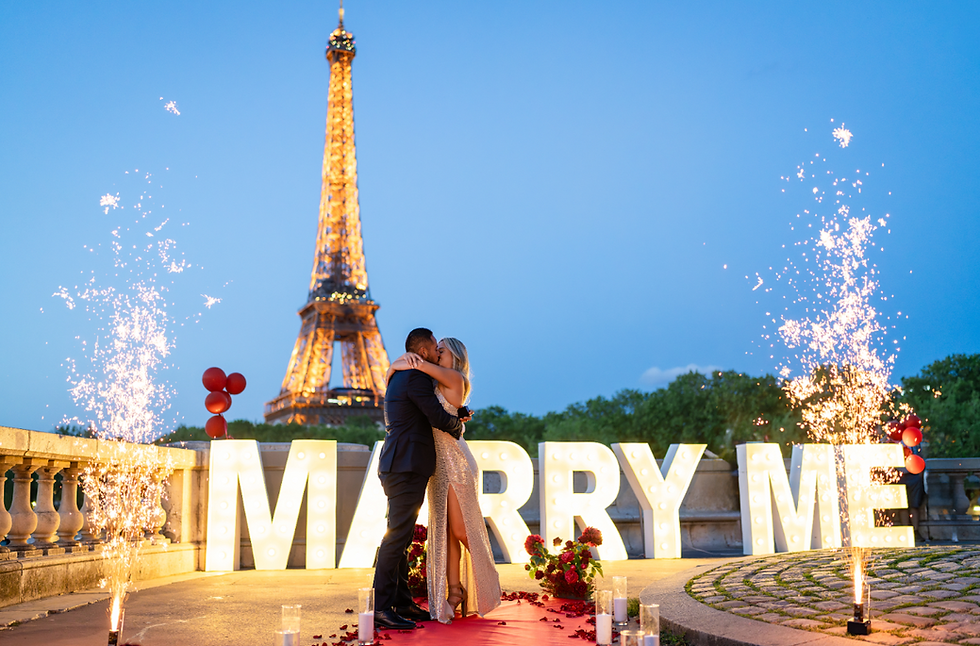 A man and woman kissing in front of the Eiffel Tower with large marry me sign, cold sparklers, roses and candles
