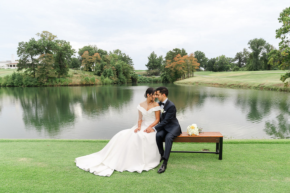 Wide-angle shot of Sarah and Vince sitting on a wooden bench overlooking the serene pond at Norwood Hills Country Club in St. Louis.
