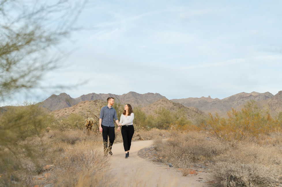 A couple walking hand-in-hand along a desert trail with a wide-angle view of the McDowell Mountains in Scottsdale, Arizona.