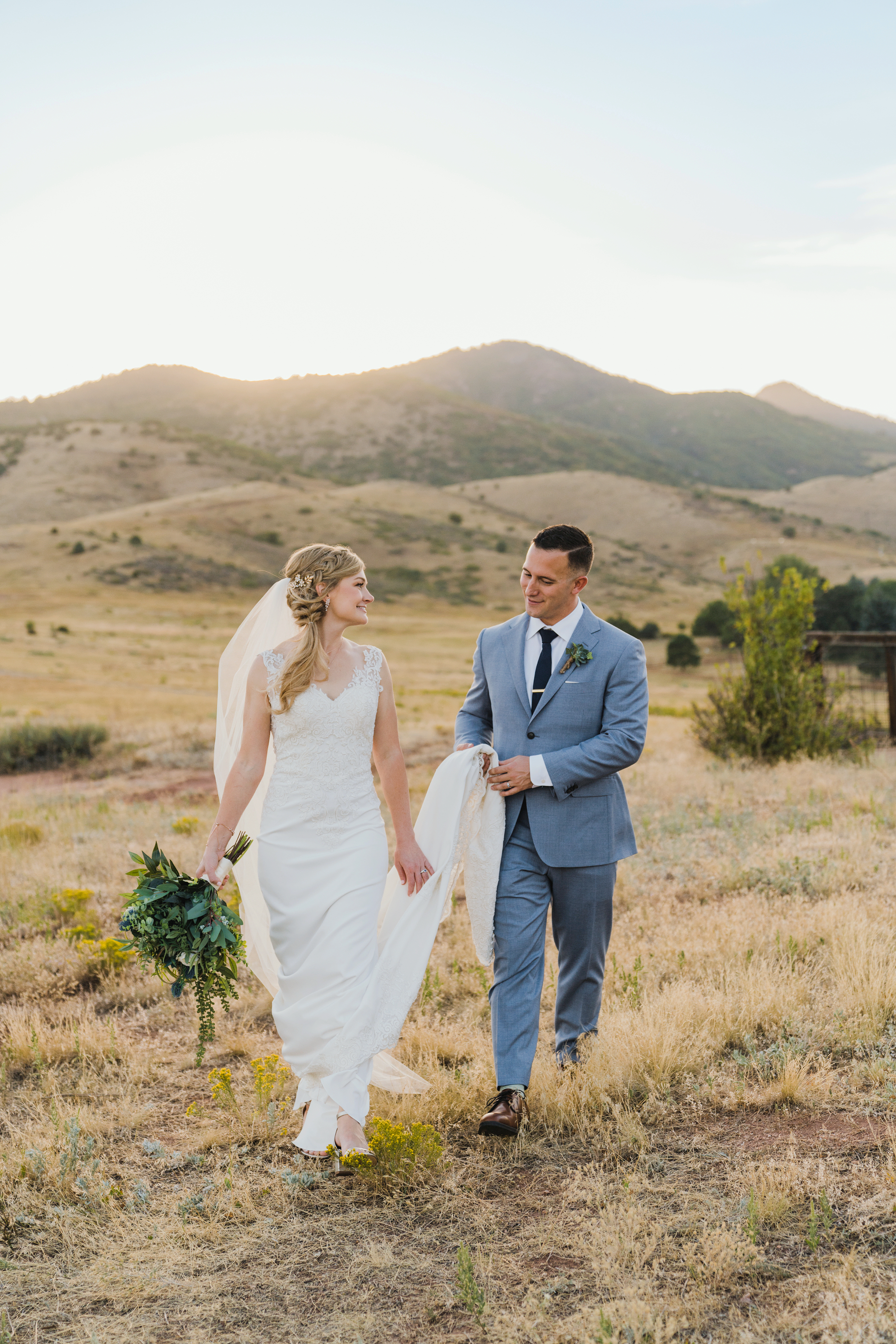 A bride and groom walking hand-in-hand through a golden mountain meadow with a view of Mount Lindo near Denver, Colorado.