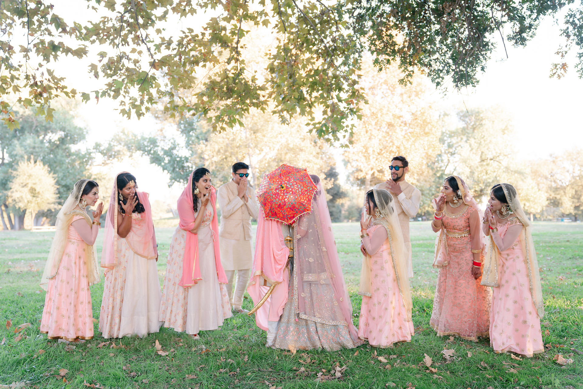 Candid moment of an Indian wedding party laughing together in a scenic Sacramento park, capturing the vibrant fashion and close-knit family energy of a South Asian celebration.