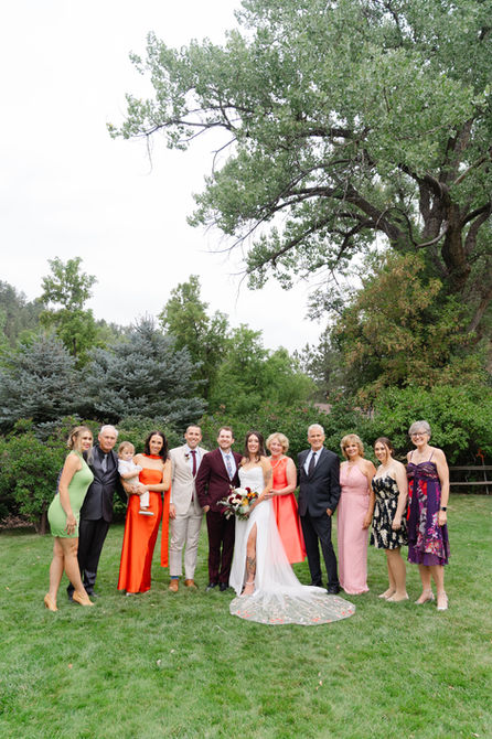 Wedding party in colorful attire posing together in a lush green park during an outdoor ceremony.