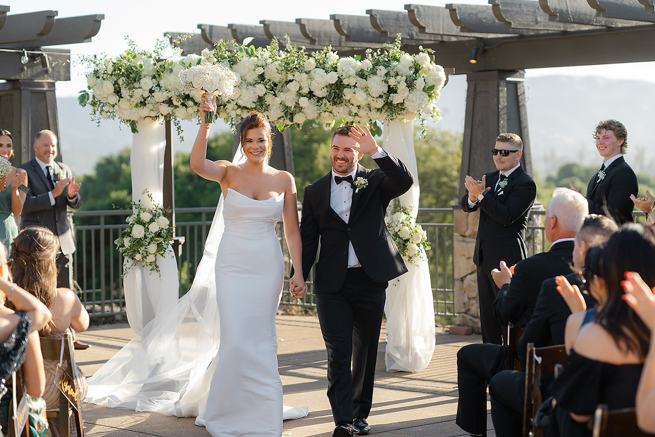 The newlyweds smiling and waving to guests while walking down the aisle at their outdoor Stone Tree Golf Club wedding.