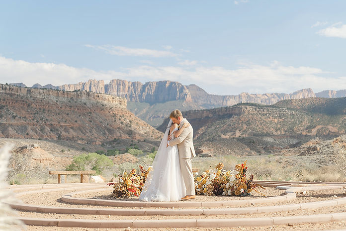 A wide-angle view of an outdoor wedding ceremony at the Zion Red Rock Villa labyrinth, featuring a circular stone ceremony site surrounded by native desert landscape and the towering red rock peaks of Southern Utah.